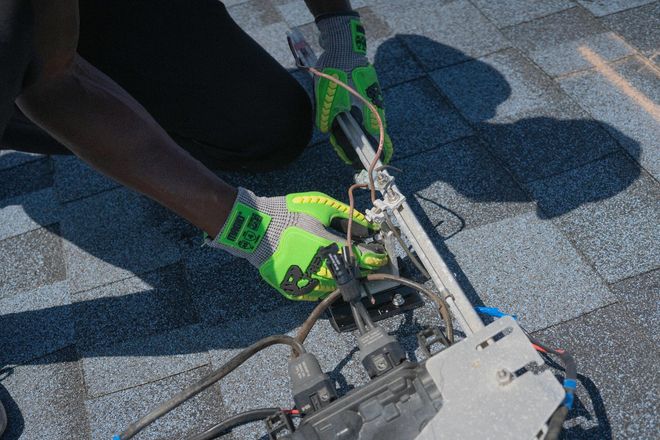 Person wearing green gloves adjusts equipment on a gray textured surface outdoors.