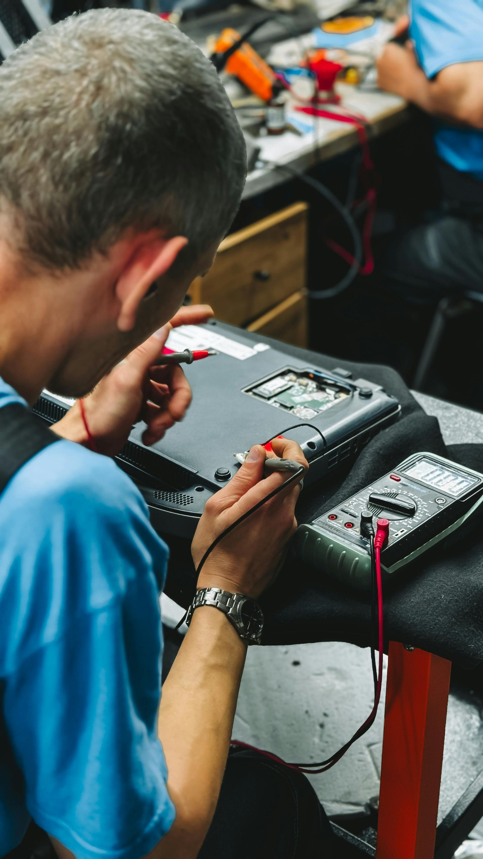 Technician repairing electronic device on a workbench with tools and wires