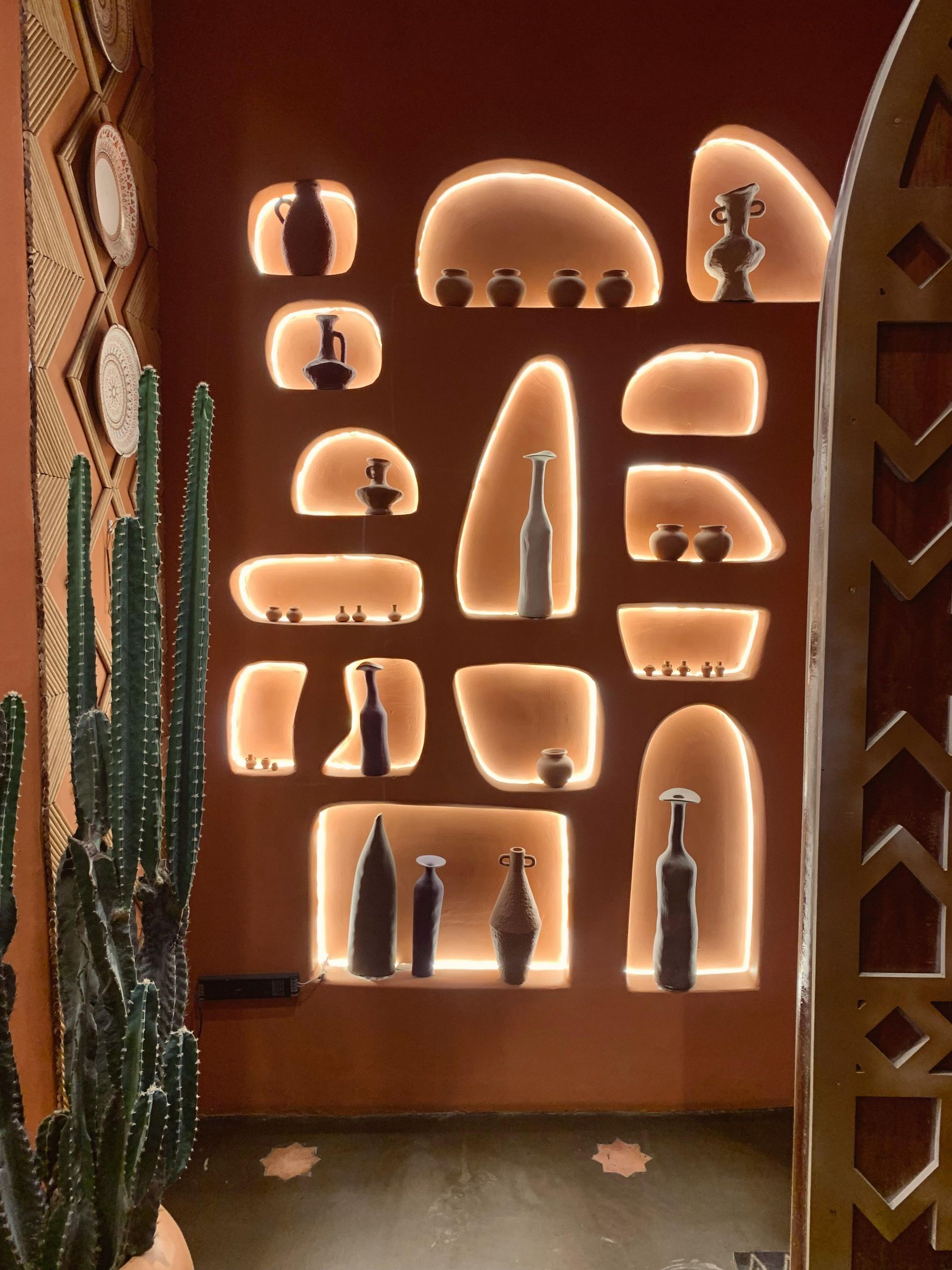 Backlit wall niche shelves displaying pottery and figurines in a warm terracotta room
