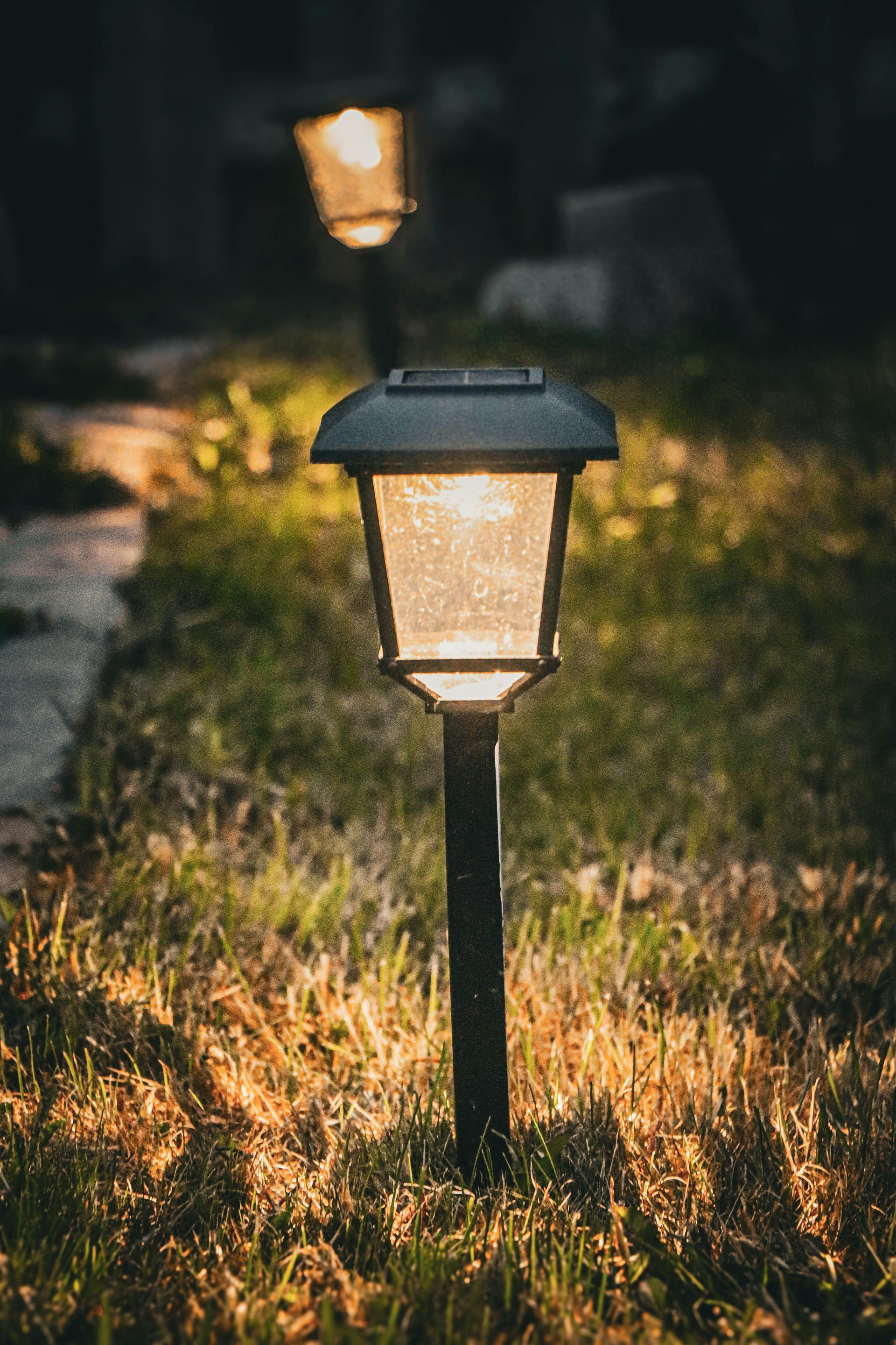 Two lit garden lanterns glowing on a grassy path at dusk