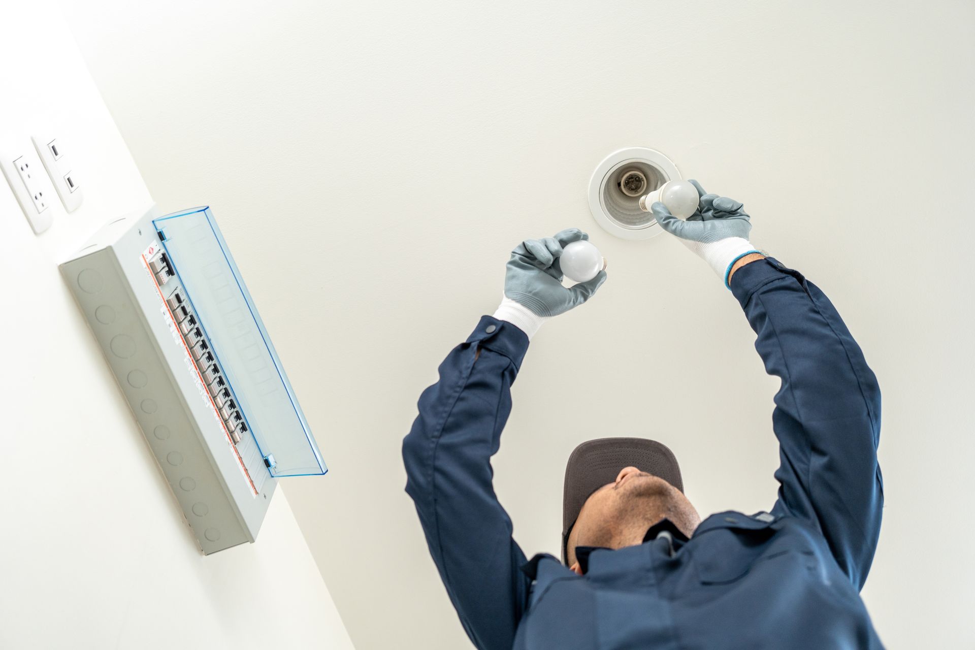Technician installing a ceiling smoke detector with a power drill.