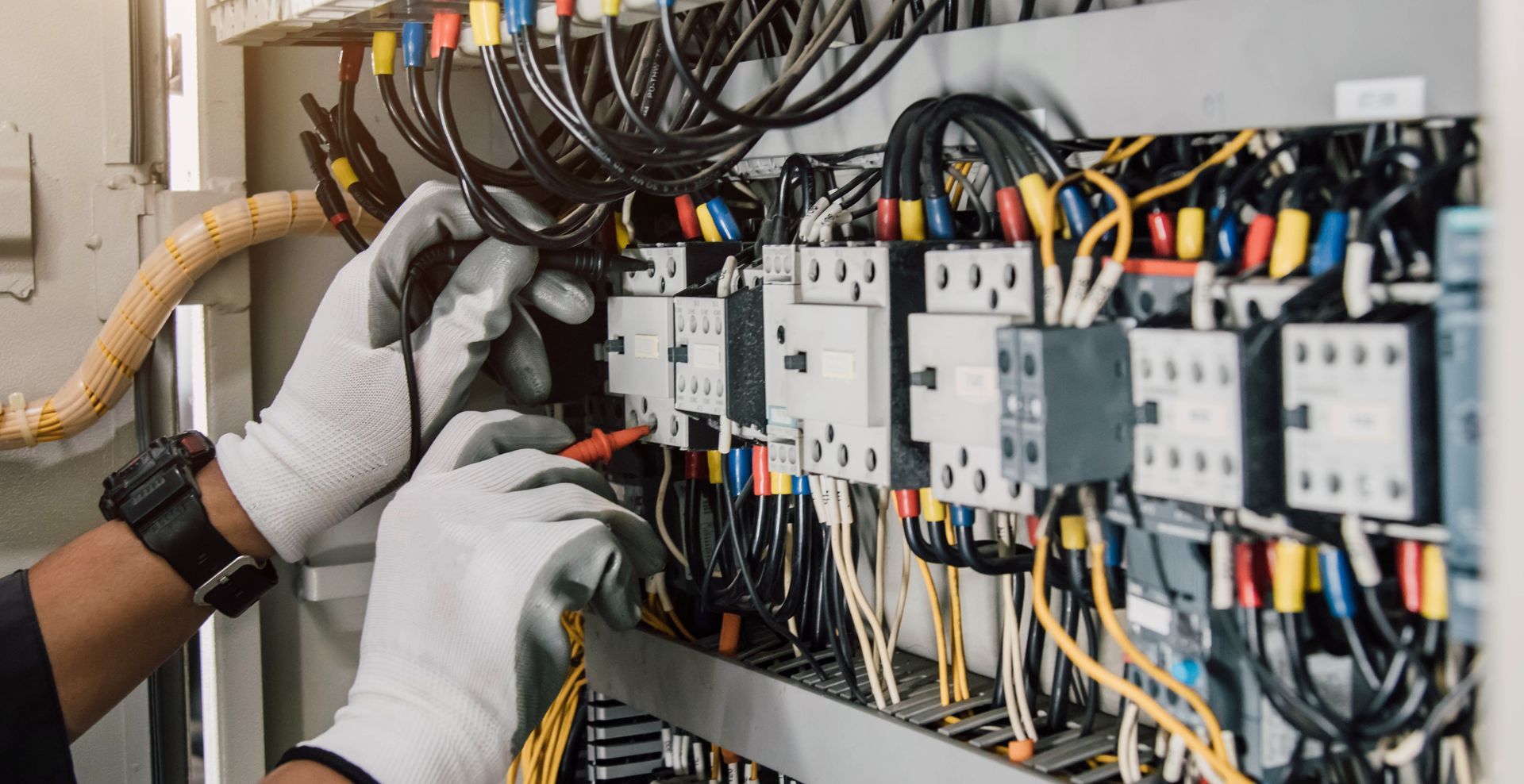 Technician wearing gloves wiring an electrical control panel with cables and circuit breakers