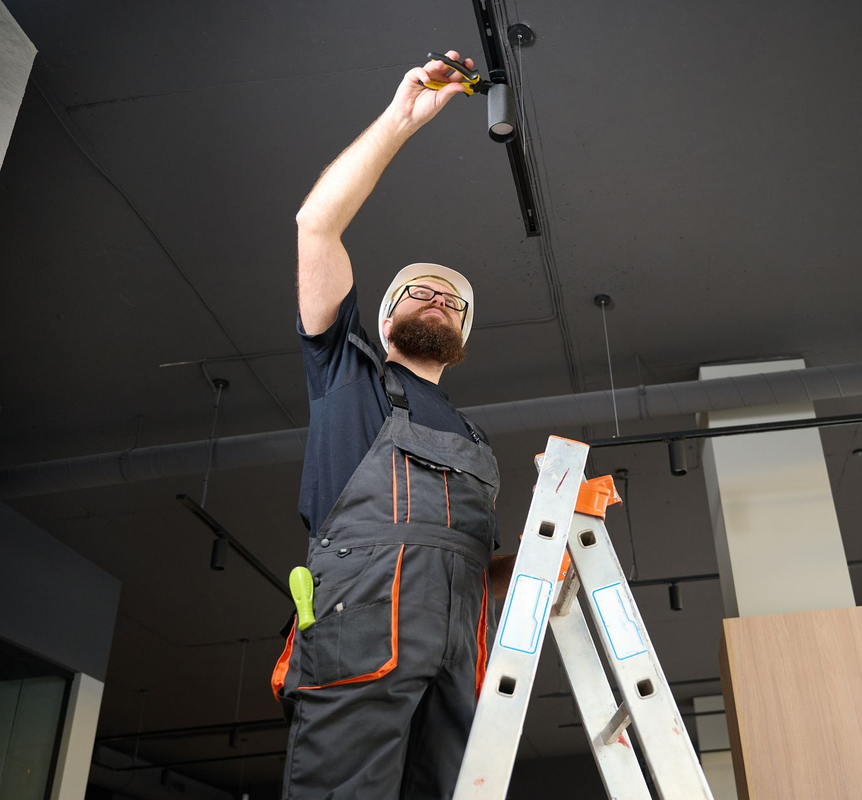 Worker on a ladder adjusting a ceiling fixture in a modern room.