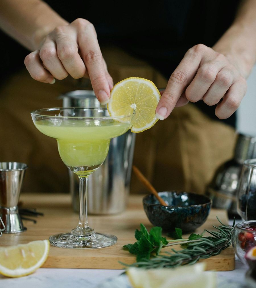 A person garnishes a margarita with a lemon slice, cocktail prep station.
