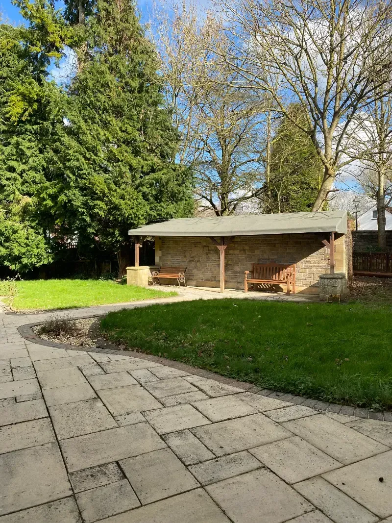 Woodlands Manor Care Home | A stone walkway leading to a shed in a park surrounded by trees.