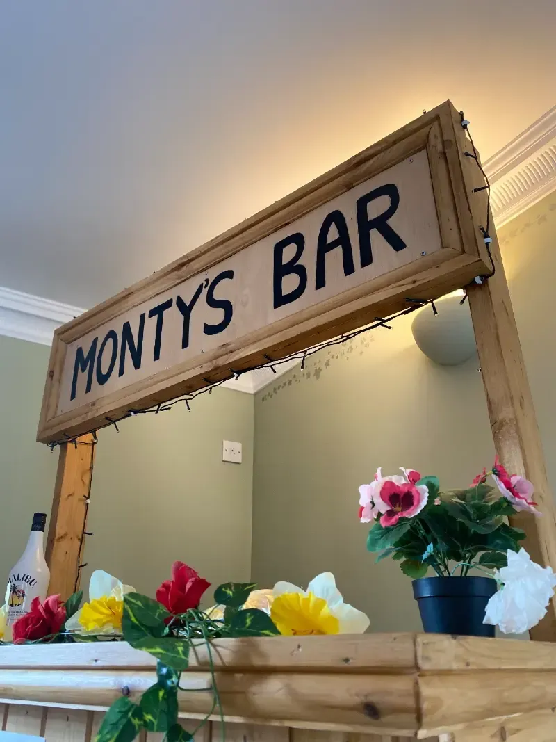 Woodlands Manor Care Home | A wooden bar with flowers and a sign that says monty 's bar