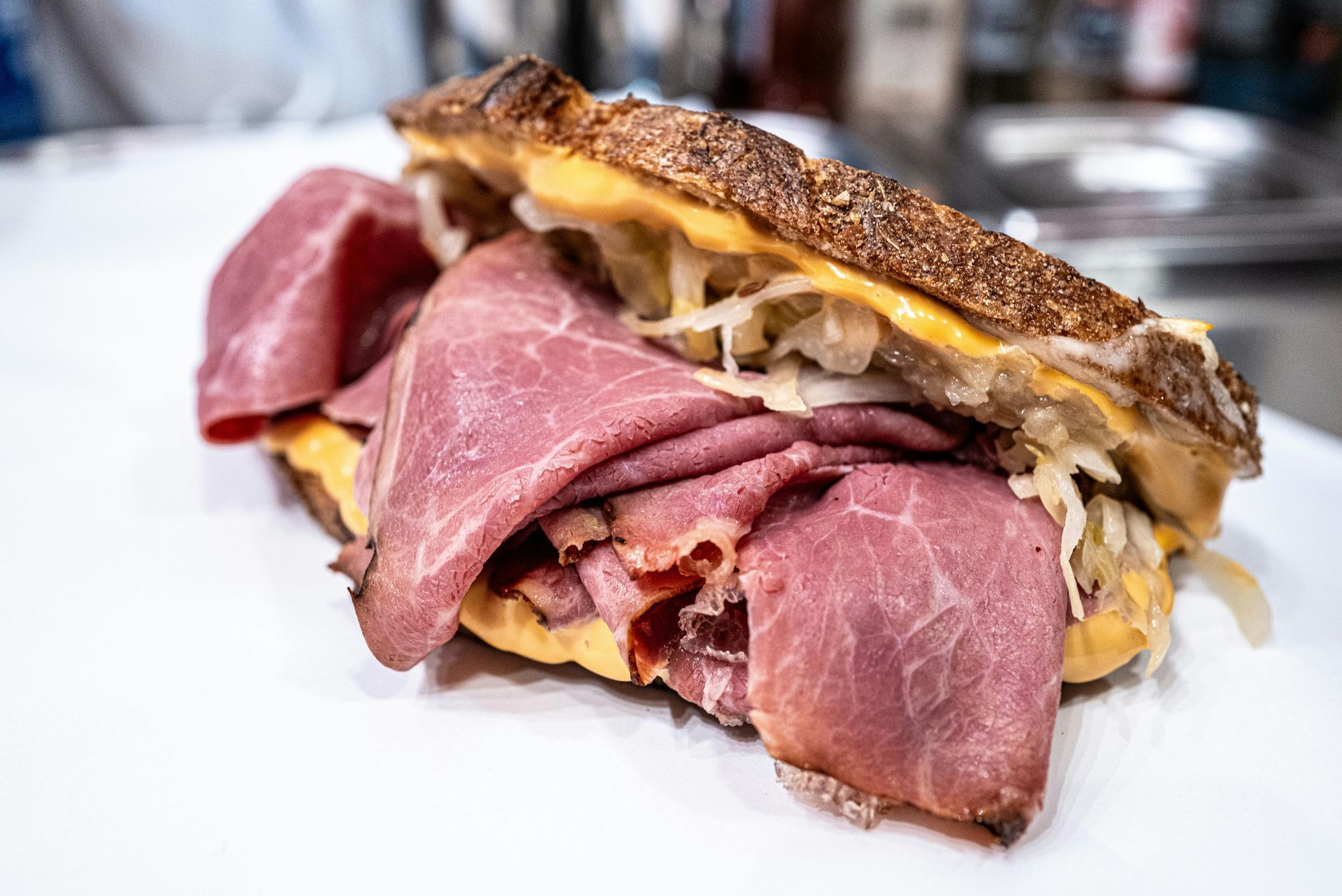 A Reuben sandwich with layers of corned beef, sauerkraut, and melted cheese on toasted rye bread on a white surface.