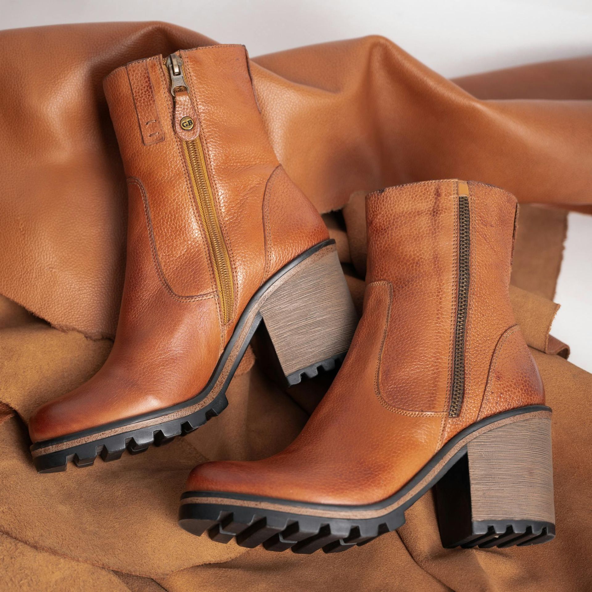 A pair of tan leather ankle boots with thick, stacked heels and rugged black lug soles, placed on brown fabric.