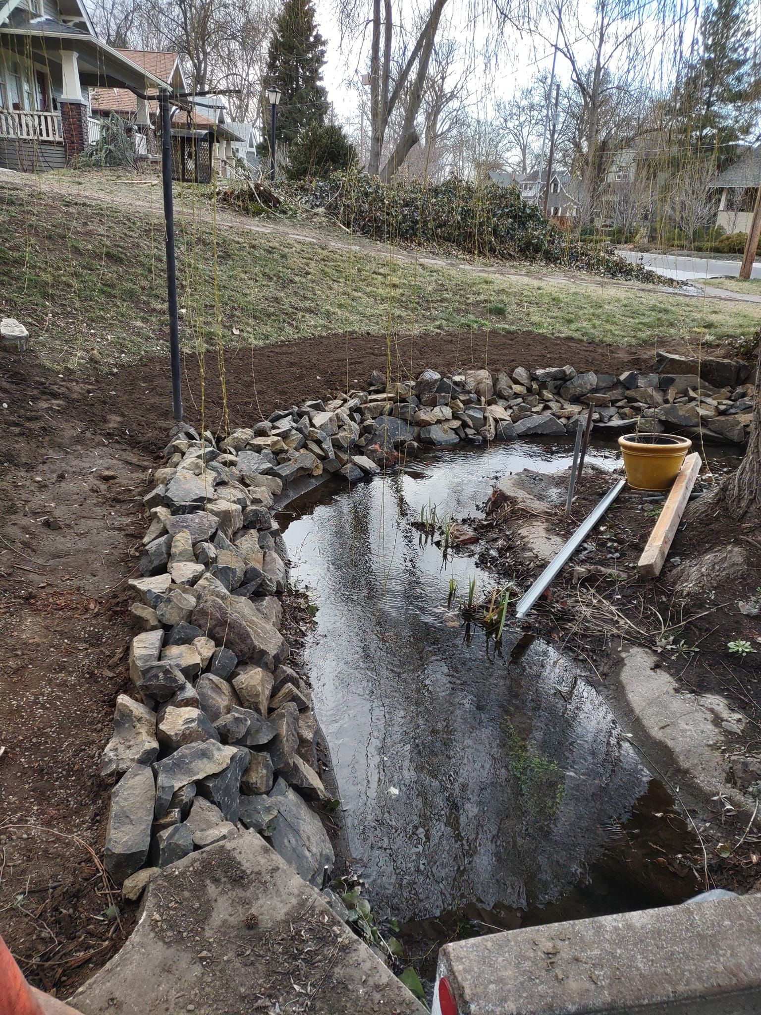 A partially constructed water feature with stone edging in a yard; various tools and materials are nearby.