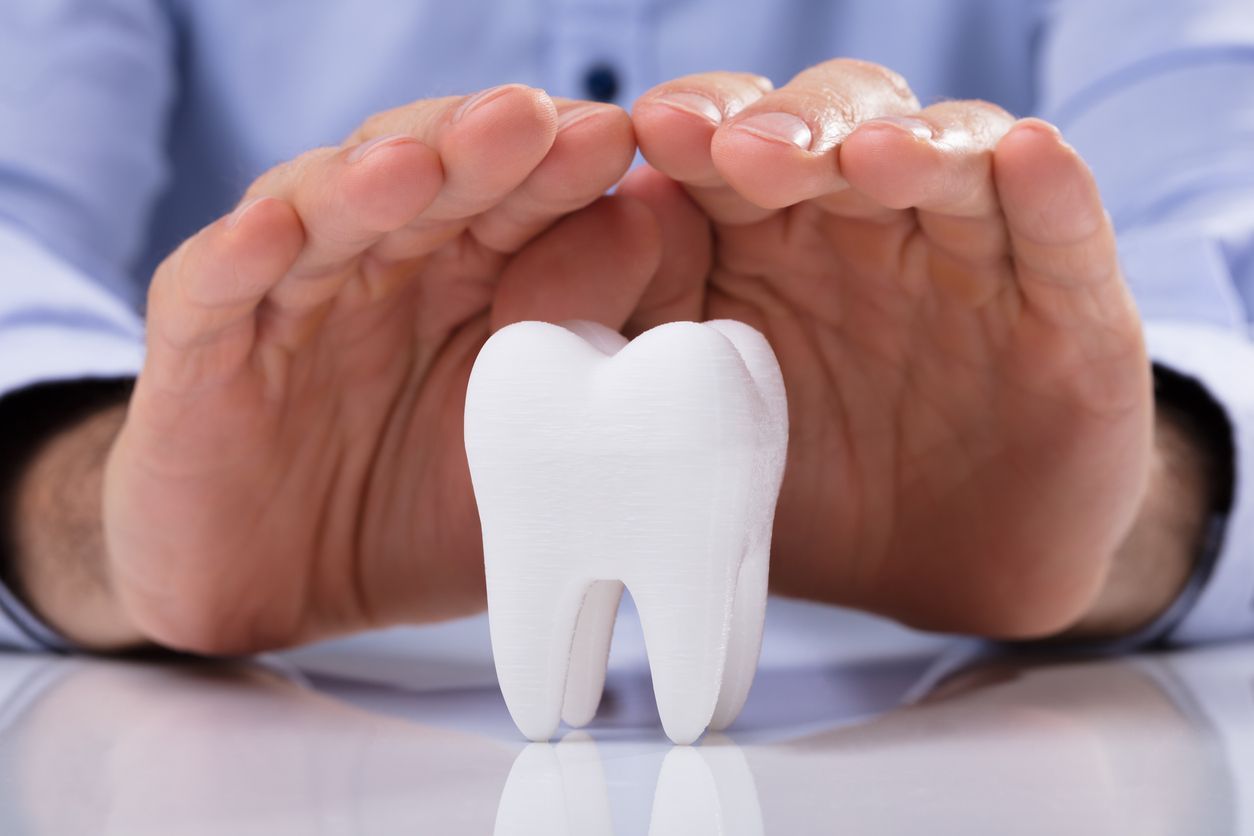 Hands cupping a white tooth, symbolizing dental care or protection.