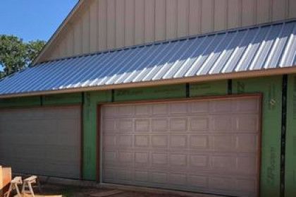 Green building with a tan garage door and blue metal roof in daylight