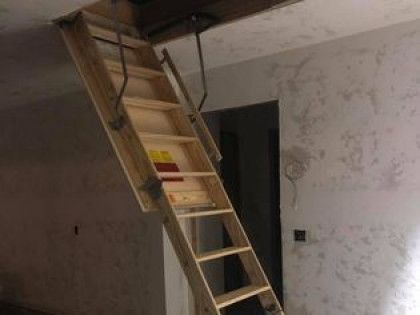 Wooden attic ladder extended in a room with unfinished walls and a doorway