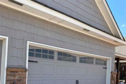 Exterior of a beige house with a white garage door and roofline visible under a blue sky