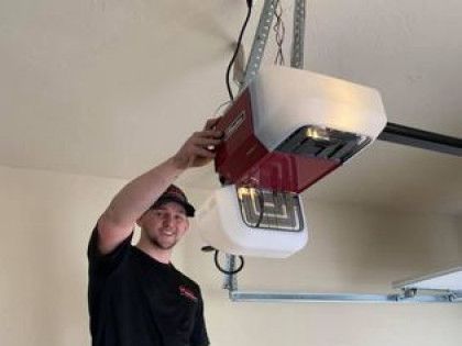 Man working on a red and white garage door opener mounted to the ceiling