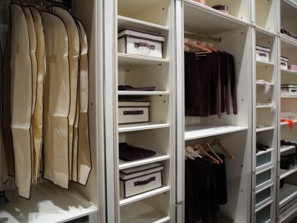 Walk-in closet with beige suits and dark clothes hanging on shelves and rods, plus folded storage boxes