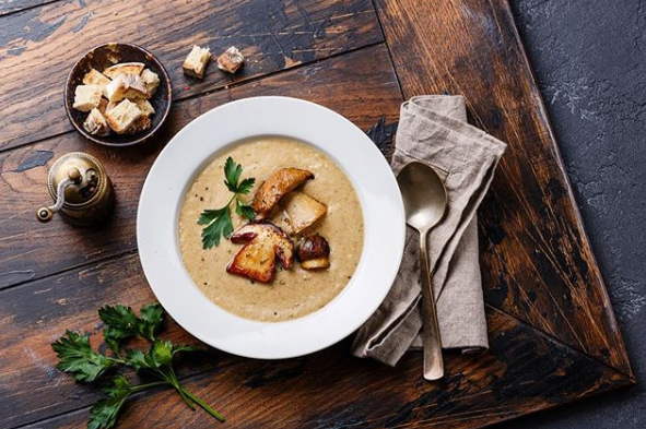 Eine Schüssel Pilzsuppe mit Croutons und einem Löffel auf einem Holztisch.