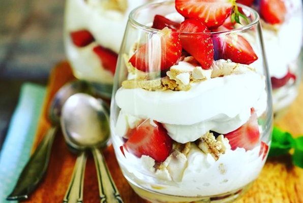 Ein Glas gefüllt mit Schlagsahne und Erdbeeren auf einem Holztisch.