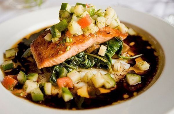 Ein weißer Teller mit einem Stück Lachs und Gemüse.