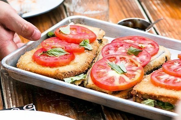 Eine Person hält ein Tablett mit Essen, auf dem Tomaten liegen.