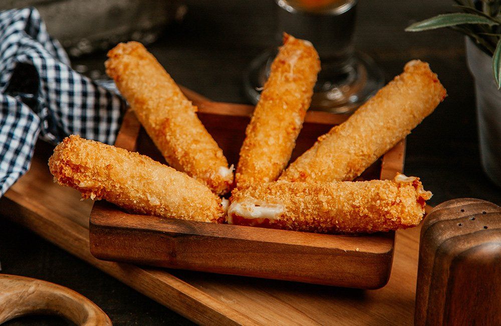A wooden tray filled with fried mozzarella sticks on a wooden table.