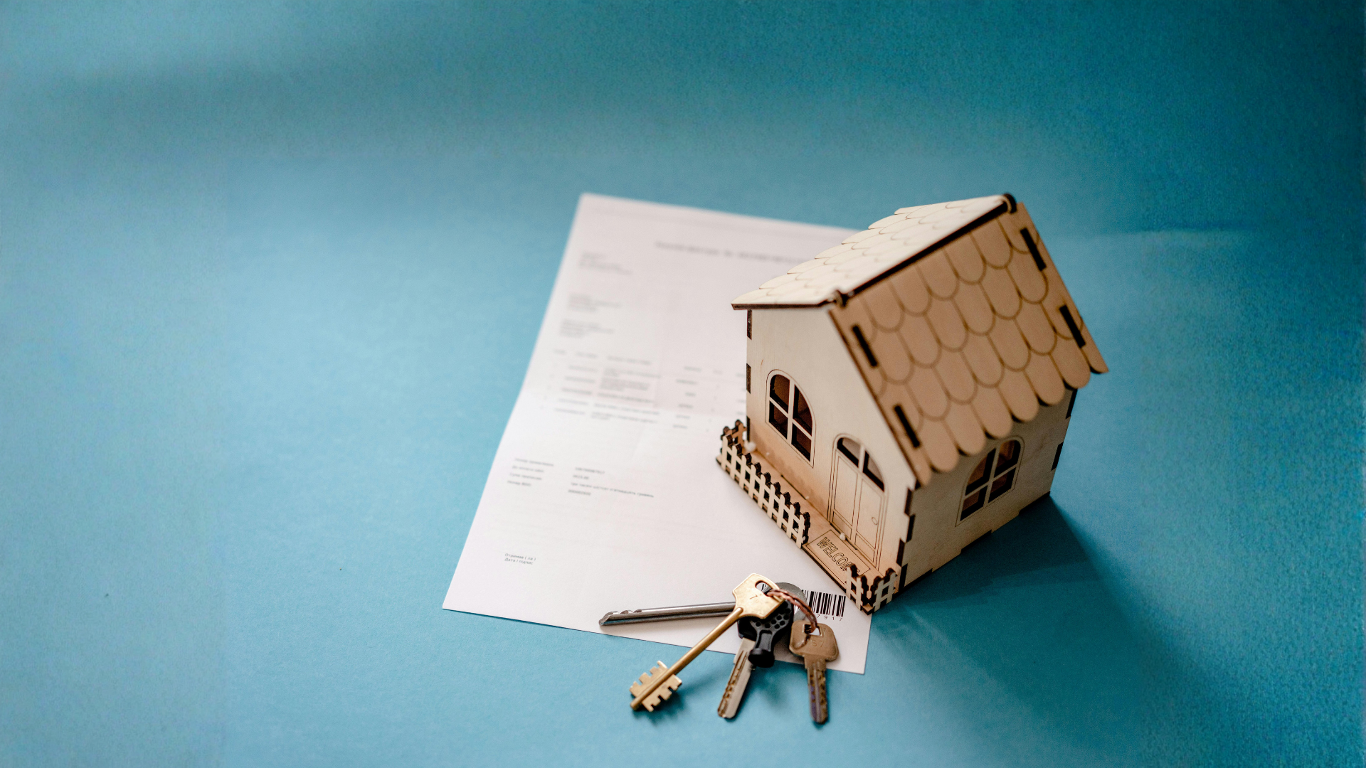 A small wooden model house sits next to a set of metal keys on top of a white paper document 