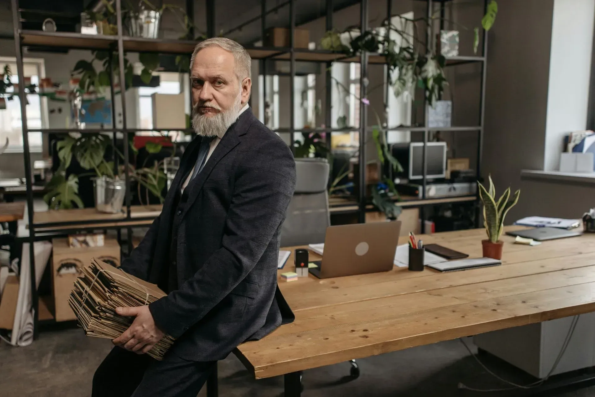 Man holding a woven basket in a modern office with shelves, plants, and a desk with a laptop