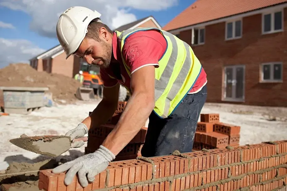 Construction worker laying bricks at a building site, wearing a hard hat and safety vest