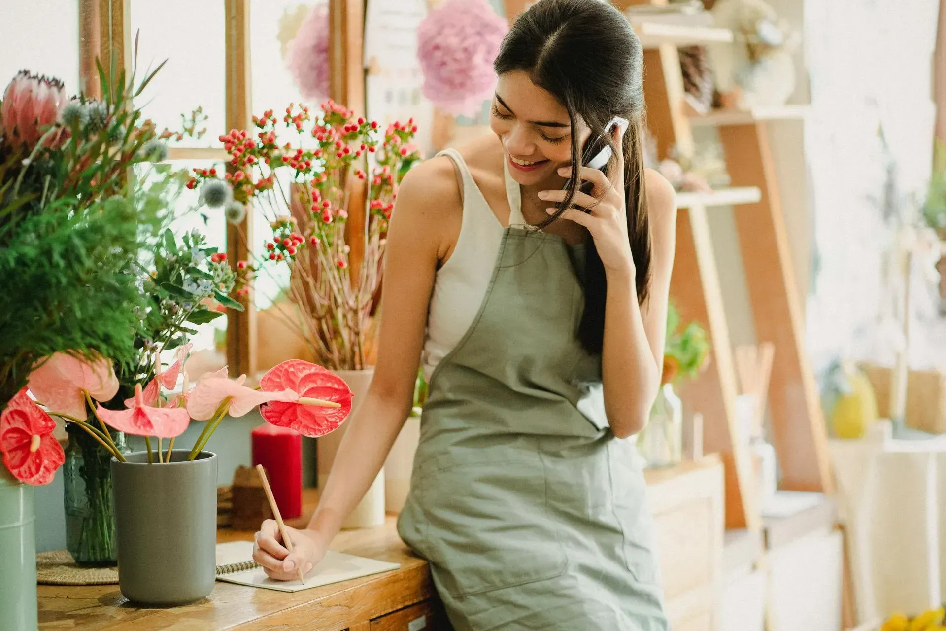 Woman in an apron talking on the phone while arranging flowers in a bright shop
