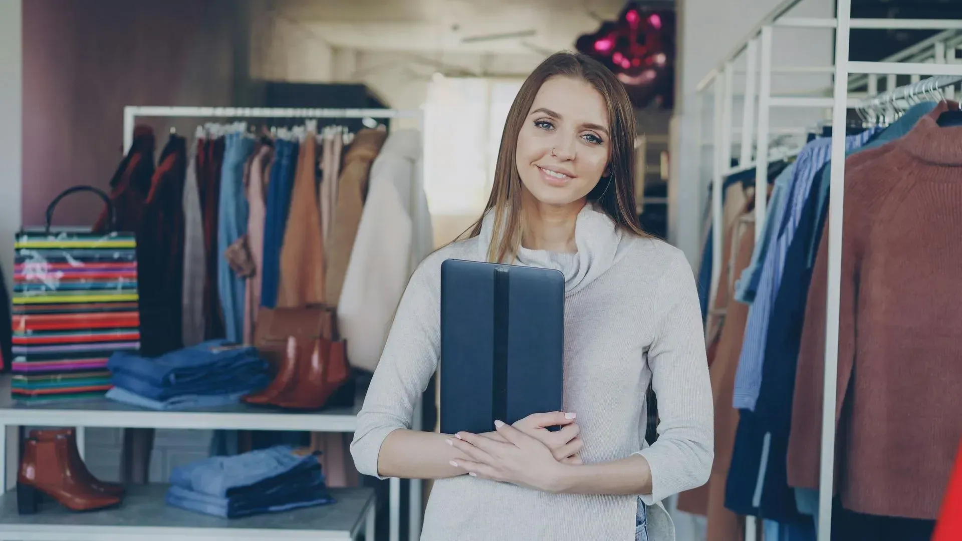 Smiling woman holding folded clothes in a clothing store with racks of garments behind her