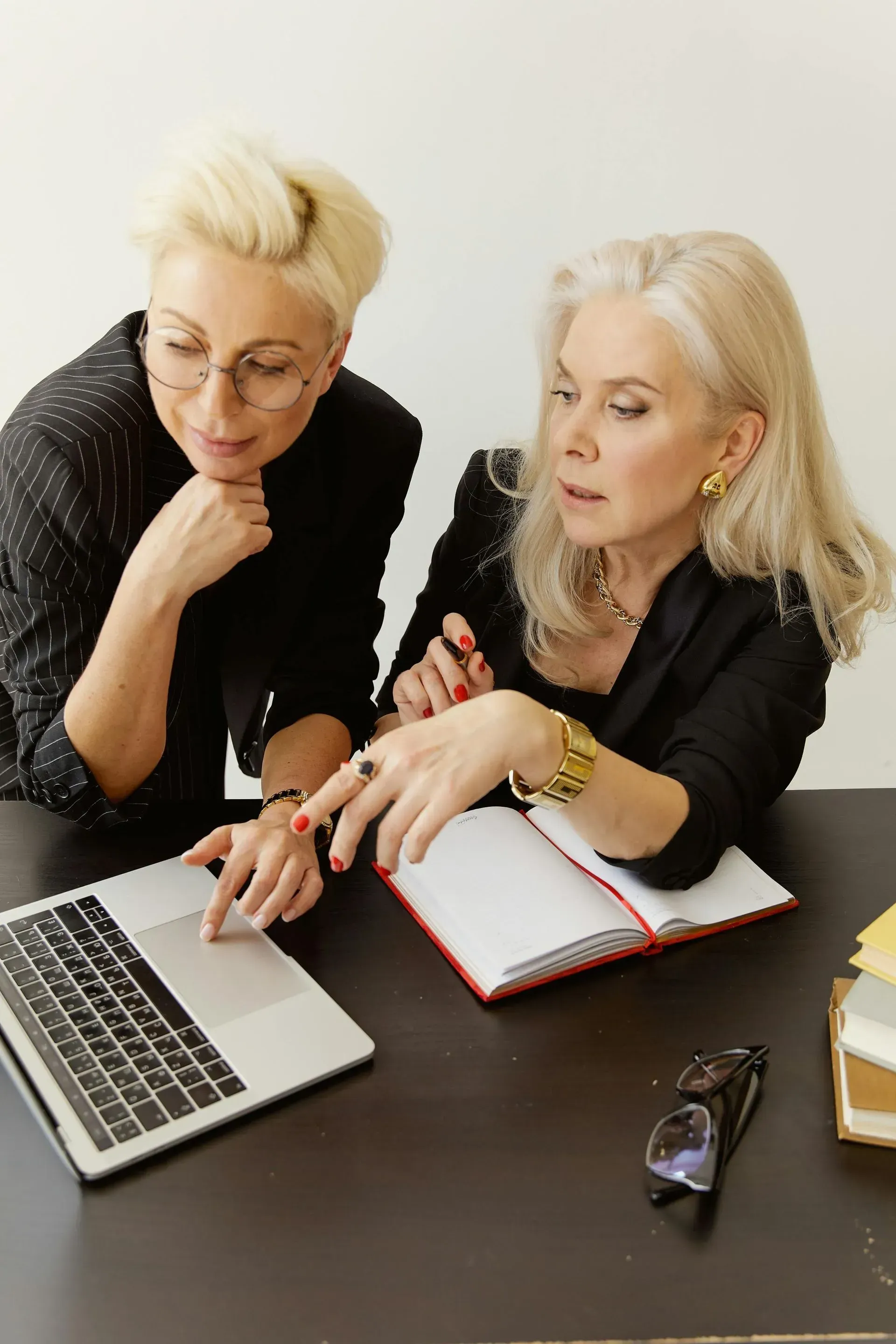Two people reviewing notes beside a laptop and notebook at a desk