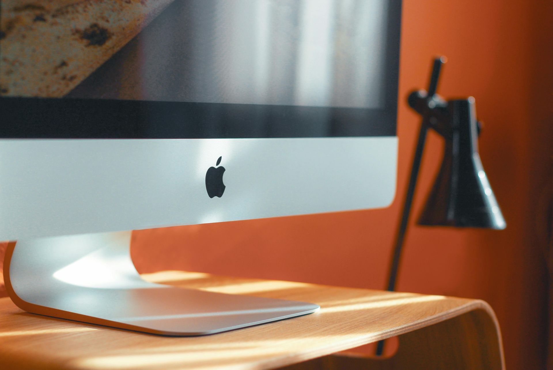 Apple iMac computer on a wooden desk with a black desk lamp.