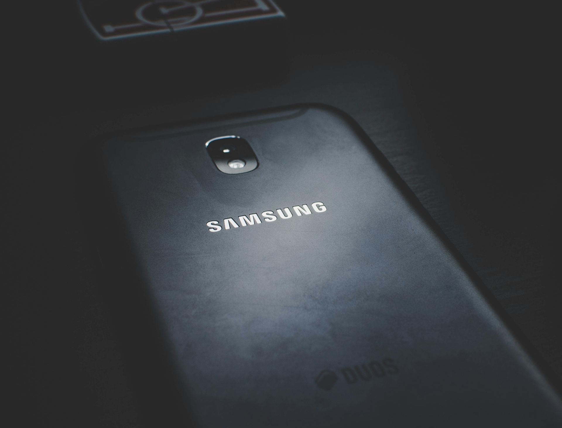 Black Samsung smartphone, back view, with camera lens and logo, on a dark surface.