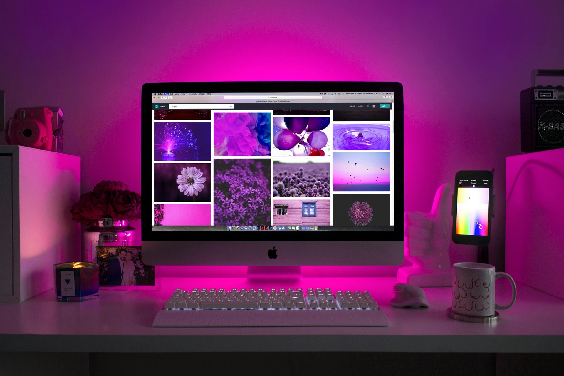 Computer desk with lit keyboard and monitor displaying purple images, bathed in pink light.