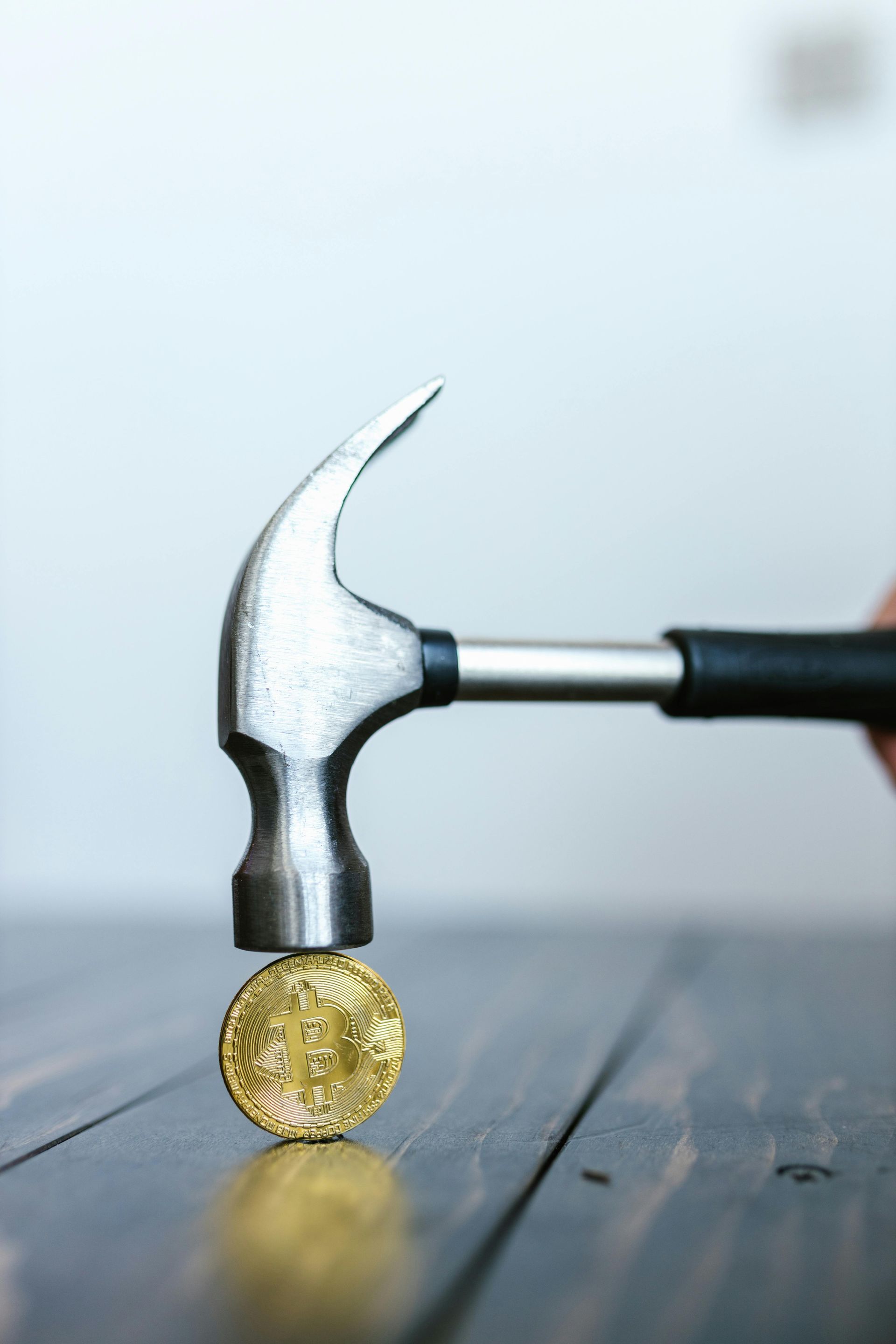 Hammer smashing a gold Bitcoin coin on a dark wood surface.