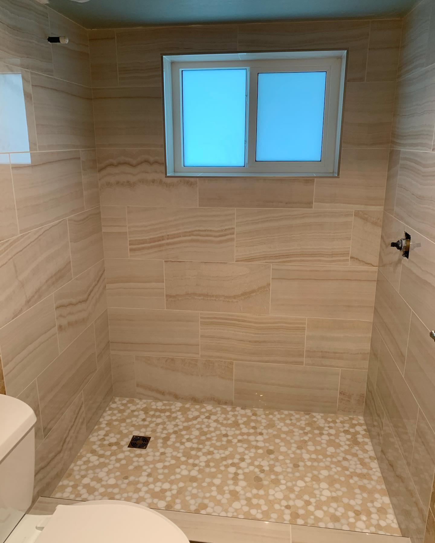 Empty tiled bathroom with a window and walk-in shower area.