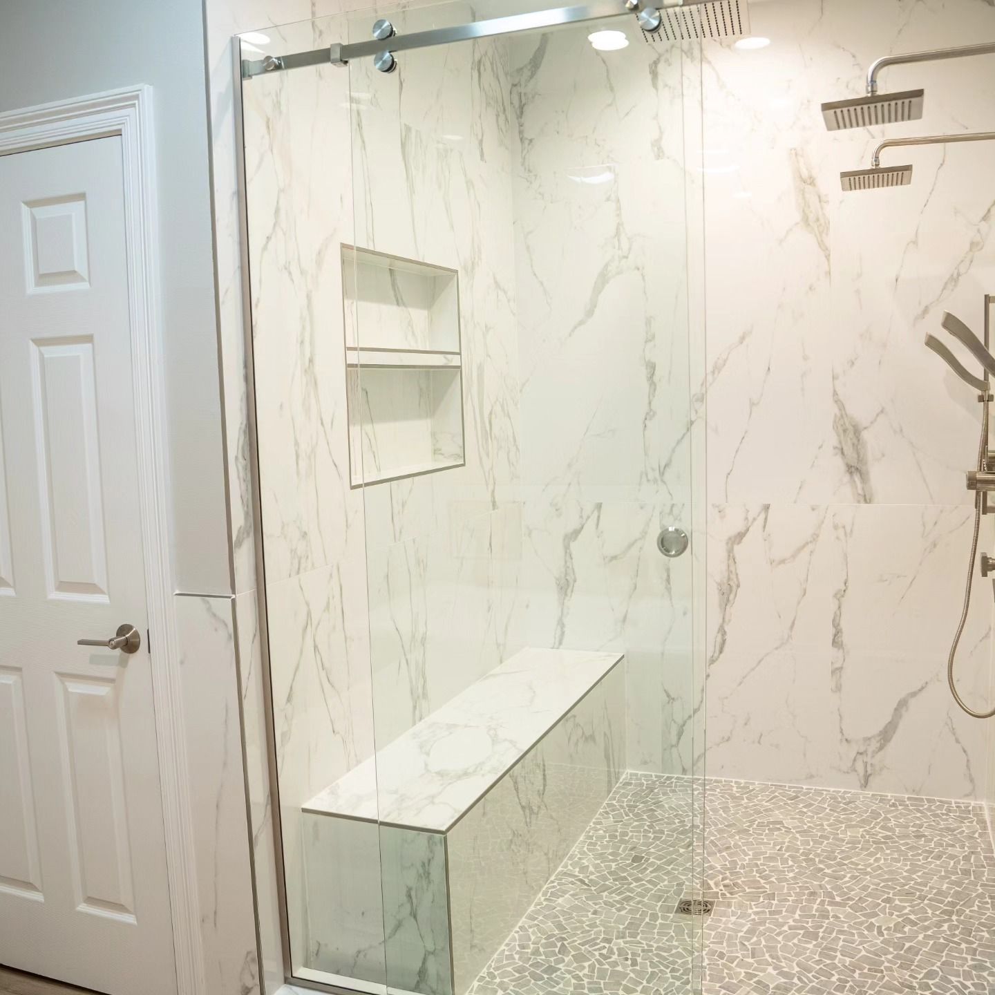 Modern bathroom shower with marble-look tile, glass enclosure, built-in bench, and pebble shower floor