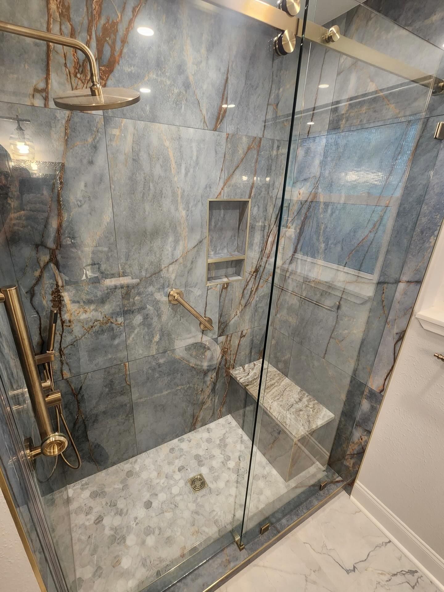 Modern shower with gray marble tile, gold fixtures, glass door, and built-in niche