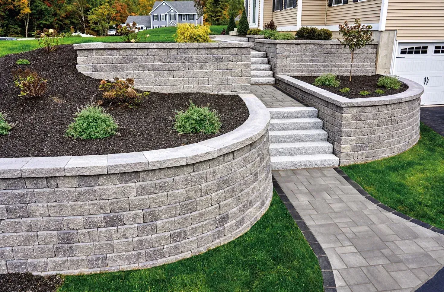 Curved stone retaining walls with stairs and a landscaped front yard beside a house