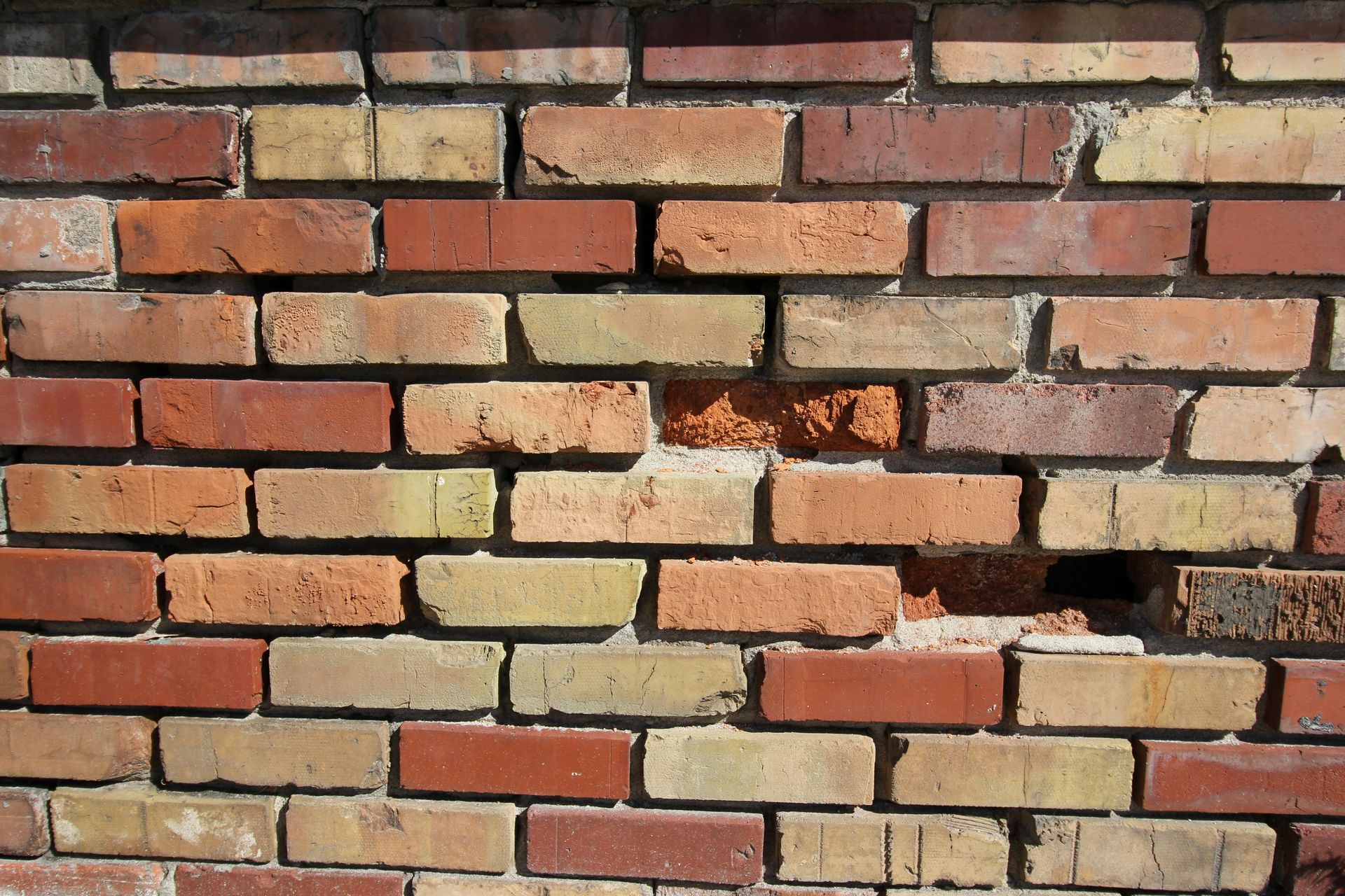 Cracked red and tan brick wall with missing and damaged bricks