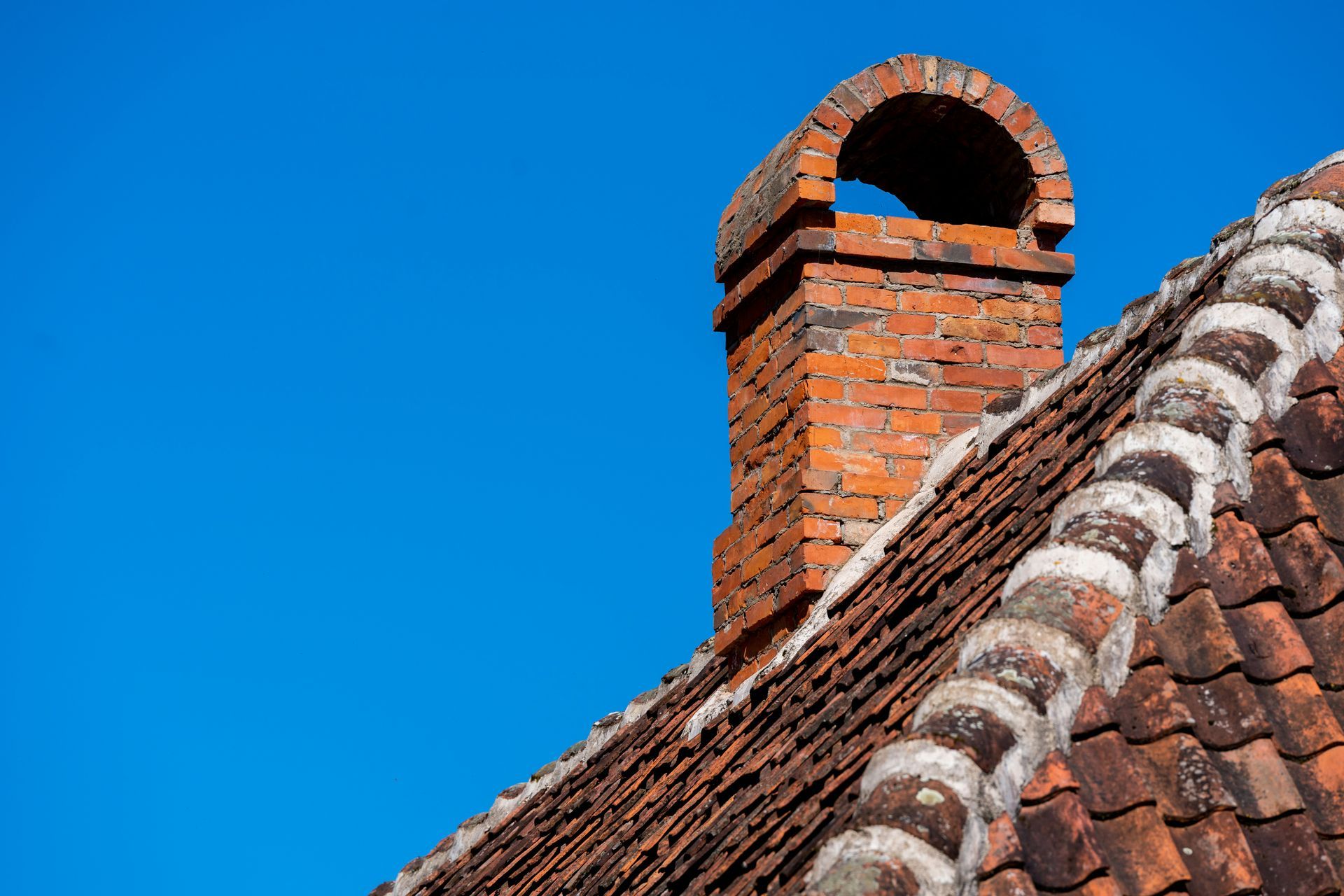 Red brick chimney on a tiled roof against a clear blue sky