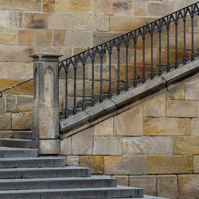 Stone staircase with black iron railing against a tan brick wall