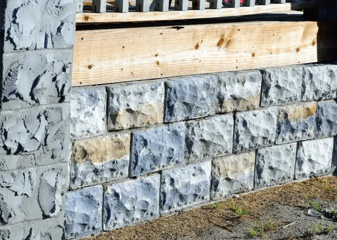 Stacked gray stone retaining wall with a wooden beam and white fence above.