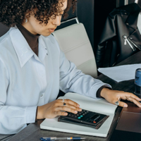 Person using a calculator at a desk beside a laptop, with notebooks and a coffee cup nearby.