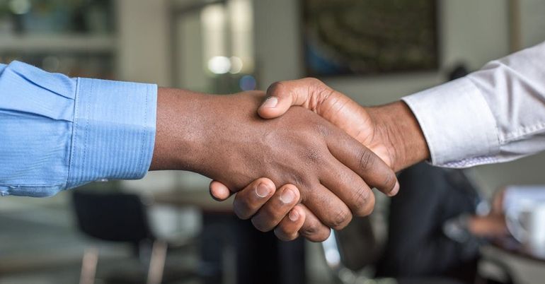 Two people shaking hands, one in a blue shirt and one in a white shirt, in an office setting