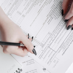 Hands writing on paperwork with a pen, reviewing documents on a desk