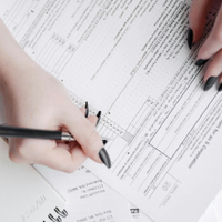 Hands writing on paperwork with a pen, reviewing documents on a desk