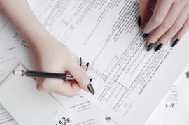 Hands with black nail polish marking up printed documents with a pen on a desk