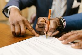 Hands pointing at a document as someone signs it with a pen at a desk