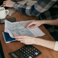 Hands reviewing printed charts at a desk with a smartphone, calculator, and coffee mug