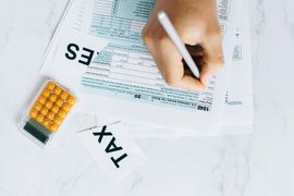 Hand writing on tax forms beside a calculator and scattered documents